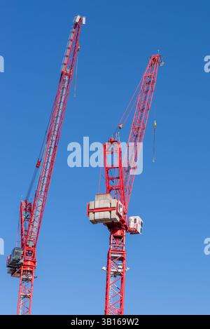 Es gibt zwei große rote Baukräne, die vor einem hellblauen Himmel stehen Stockfoto