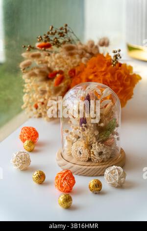Eine wunderschön angeordnete Kuppel aus konservierten getrockneten Blumen auf einem Holzsockel, umgeben von dekorativen Kugeln, die eine warme und rustikale Note von Elega schaffen Stockfoto