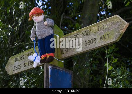 Yarnbombe Person am Fingerpfosten befestigt (öffentlicher Fernwanderweg, Ebor Way, Dales Way Link) Nahaufnahme - Menston, West Yorkshire, England Großbritannien. Stockfoto