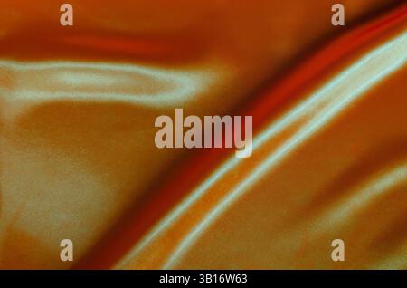 Draufsicht auf dunkelorangefarbene Seide mit weichen Kurven und leuchtender reflektierender Oberfläche. Geeignet für Design und Hintergrundtapeten. Stockfoto