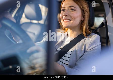 Junge schöne Geschäftsfrau, die glücklich ein modernes Auto mit Händen am Lenkrad fährt. Stockfoto