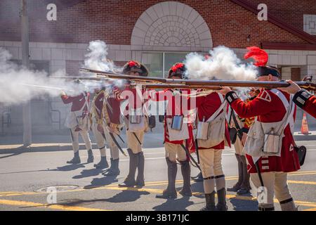 Arlington, MA, USA-20. April 2025: Battle of Menotomy 250th Reenactment – patriotische Kolonialisten kämpfen gegen britische Soldaten auf der Massachusetts Avenue. Stockfoto