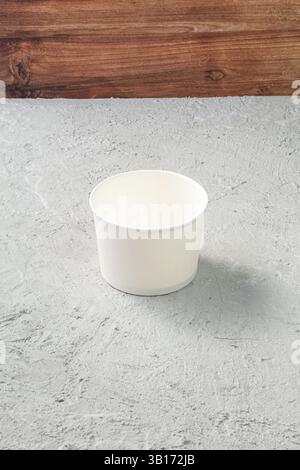 Leere weiße Papierschüssel auf Beton strukturierter Tisch mit hölzernem Hintergrund, rustikale minimalistische Küchenszene für Food Mockup oder Geschirr Display mit Co Stockfoto