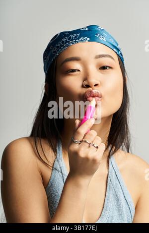 In einem modernen Studio trägt eine junge Frau spielerisch hellen Lippenstift auf, der Selbstvertrauen ausstrahlt. Stockfoto