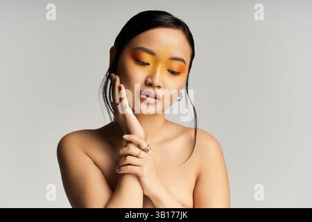 Eine junge asiatische Frau posiert elegant mit leuchtendem gelbem Augen Make-up und Selbstvertrauen. Stockfoto