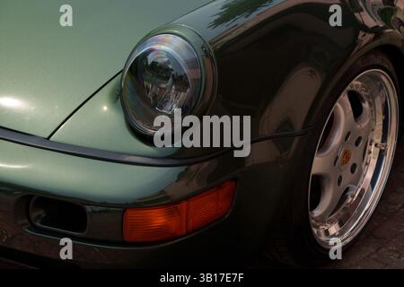 Nahaufnahme des Frontscheinwerfers, der Blinkleuchte und der Leichtmetallfelge eines klassischen dunkelgrünen Porsche 911, der auf einem Ziegelpflaster geparkt ist. Stockfoto