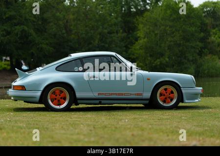 Ein klassischer, hellblauer Porsche 911, der auf Gras geparkt ist, Seitenansicht, mit schlankem Design und orangefarbenen Details. Stockfoto