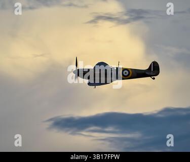 Ein einsitziges Supermarine Spitfire Kampfflugzeug schwingt vor dem Hintergrund dramatischer Wolken während eines Sonnenuntergangs in Duxford, England. Stockfoto