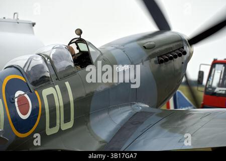 Ein Supermarine Spitfire-Kampfflugzeug aus dem Zweiten Weltkrieg mit der Bezeichnung „Gallagher“ sitzt auf dem Flugplatz, dessen Pilot im Cockpit von Duxford, England, sichtbar ist. Stockfoto