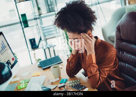 Junge professionelle Frau in stilvoller Bürokleidung, die Stress an ihrem Arbeitsplatz erlebt, umgeben von Geschäftsmaterialien Stockfoto