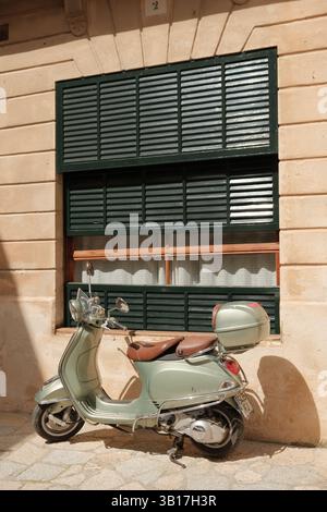 Vintage mintgrüner Vespa Roller, der vor einem traditionellen mediterranen Gebäude mit grünen Fensterläden geparkt ist. Stockfoto