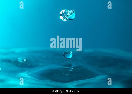 Wassertropfen fallen dicht in das blaue Wasser, was es zum perfekten Zentrum in der Natur macht Stockfoto