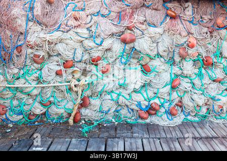 Ein großer Stapel von Fischernetzen mit Schwimmern liegt auf einem Holzsteg gesammelt. Stockfoto