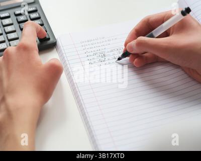 Ein Schüler, der Mathematik in einem Notizbuch mit einem Taschenrechner macht. Nahaufnahme. Stockfoto