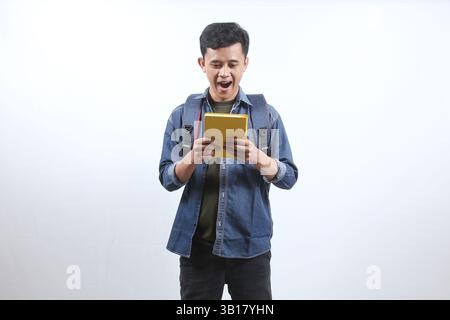 Asiatischer Mann mit dunkelblauem Denim-Hemd mit Rucksack und Geschenkbuch glücklicher Ausdruck, isoliert auf weißem Hintergrund. Bildungskonzept Stockfoto