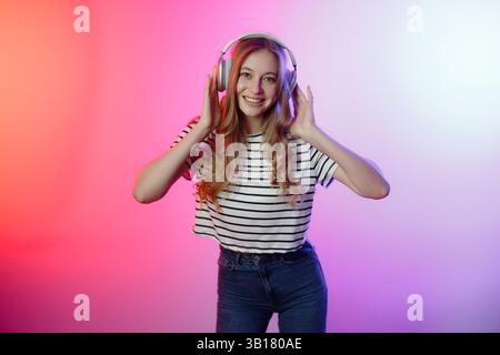 Junge Frau, die Musik mit Kopfhörern in farbenfrohem Umgebungslicht genießt Stockfoto