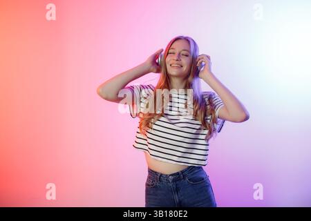 Junge Frau, die Musik genießt, während sie Kopfhörer in farbenfroher Beleuchtung trägt Stockfoto