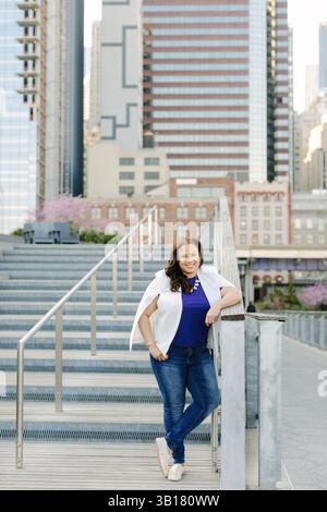 Frau in legeren Kleidern steht auf Stufen und genießt den Blick auf die Stadt unter hellem Himmel im pulsierenden Stadtzentrum. Stockfoto