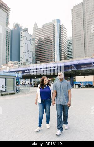 Ein fröhliches Paar spaziert Hand in Hand durch ein pulsierendes Stadtbild, umgeben von hohen Gebäuden und urbanem Leben. Stockfoto