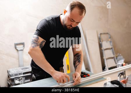 Builder preparing aluminum profiles for stretch ceiling using special equipment in apartment being renovated Stockfoto