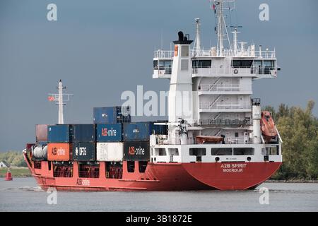21. April 2025: Puttershoek-Niederlande: Rotes Frachtschiff A2B Spirit transportiert Container entlang der Oude Maas unter bewölktem Himmel. Stockfoto