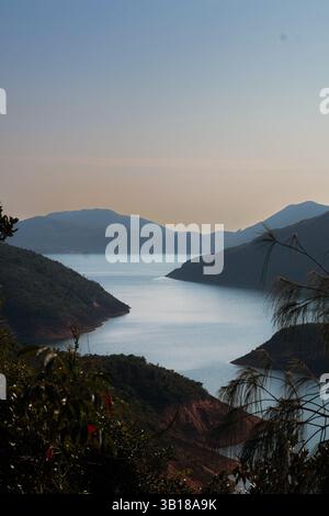 Ruhiger Blick auf die Natur mit einem weiten Abschnitt Wasser von oben und Silhouetten von kleinen Bergen im Hintergrund unter einem friedlichen Himmel. Stockfoto