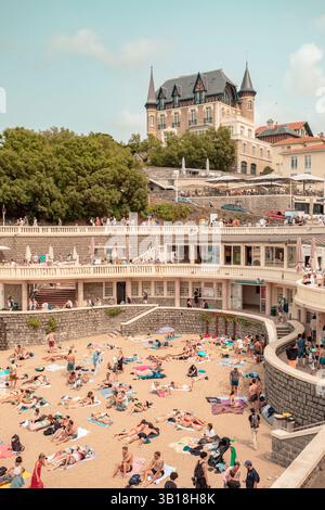 Plage du Port Vieux in Biarritz, Baskenland, Frankreich, mit Menschen, die sich am Sandstrand entspannen und im ruhigen Wasser der geschützten Bucht schwimmen Stockfoto