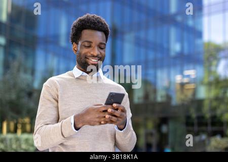 Junger erfolgreicher Geschäftsmann, der mit einem Telefon in der Hand durch die Stadt geht, schreibt eine Textnachricht und durchsucht soziale Netzwerke im Internet. Firmenmitarbeiter zur Mittagszeit. Stockfoto
