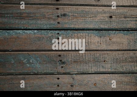 Eine Nahaufnahme alter Holzdielen mit verblasster blauer Farbe und sichtbaren Rissen. Die raue Textur, die verstreuten Nägel und die abblätternde Farbe betonen das rustikale Stockfoto