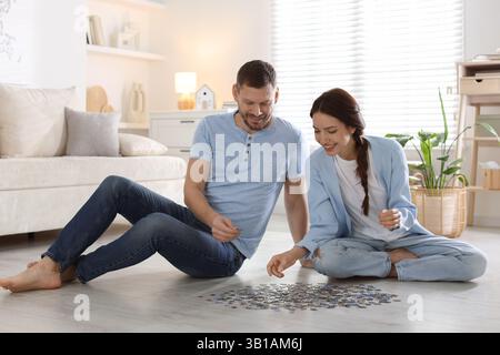 Glückliches Paar löst zusammen Puzzle auf dem Boden drinnen Stockfoto