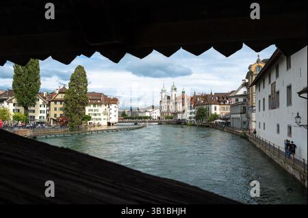 Luzern, Schweiz - 7. Juli 2024: Blick auf eine Reuss mit historischen Gebäuden von Luzern, eine Brücke im Hintergrund, eingerahmt von einem Holzbau Stockfoto