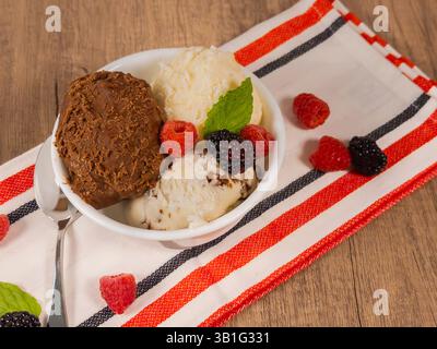Eine Vollformataufnahme einer Schale Eis mit Vanille und Schokolade, die auf einem Tisch mit Beeren sitzt Stockfoto