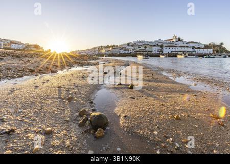 Sonnenaufgang am Atlantik, Skyline eines Fischerdorfes hinter einem Hafen. Sandstrand bei Sonnenaufgang. Landschaftsfotografie in Ferragudo, Portimao, Algar Stockfoto