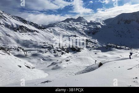 Skifahrer stehen auf einem verschneiten Berghang mit malerischem Schnee - bedeckte Gipfel im Hintergrund unter einem blauen Himmel mit Wolken. Österreich - Obertauern Stockfoto