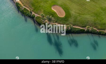 Blick über der Drohne direkt auf einen Golf Green Komplex mit Blick auf das Grün, einen großen umliegenden Sandbunker und den Rand einer blauen Lagune Stockfoto
