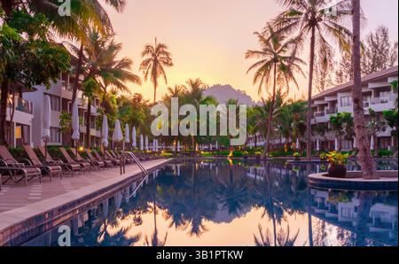 Wunderschönes Panorama bei Sonnenaufgang über einem tropischen exotischen Hotel unter hohen grünen Palmen. Reflexion der Morgensonne und Palmen im kristallklaren Licht Stockfoto