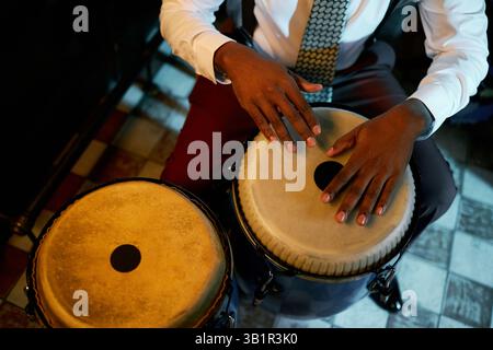 Beschnittene Aufnahme eines männlichen Musikers in stilvollem Anzug mit Tie, der Beat auf traditionellen Conga-Trommeln spielt, während er in der Bar unter Neonlichtern afro-kubanische Jazzmusik aufführt Stockfoto