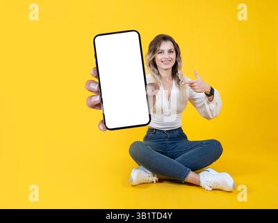 Wunderschönes weißes blondes Mädchen mit Zahnspangen, das einen großen, leeren Bildschirm des Mobiltelefons zeigt, stellt sich ganz nah vor der Kamera vor. Zeigender Touchscreen. Stockfoto