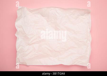 Zerknittertes Stück weißes Pergament oder Backpapier auf rosa Hintergrund. Kopierbereich für Text und Designelement. Draufsicht Stockfoto