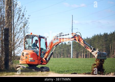 Mir, Weißrussland - 7. April 2025: JCB 8035 ZTS Minibagger mit Arbeiter im Grabboden auf dem Feld. Graben für Kabel oder Rohrleitungen. Stockfoto