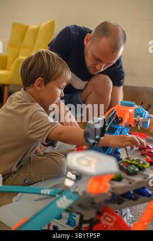 Vater und Sohn spielen zu Hause auf der Rennstrecke. Glücklicher Bindungsmoment, Kinderfreude und Familienzeit mit Spielzeugautos in gemütlichem Wohnzimmer Stockfoto