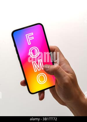 Die Hand hält ein Smartphone mit dem Wort FOMO (Angst vor dem Verpassen) – sucht nach sozialen Medien, Angst, wichtige Updates zu verpassen Stockfoto