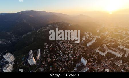 Luftaufnahme einer Stadt bei Sonnenuntergang in der Nähe von Bergen, die von Drohnen erfasst wird und eine Mischung aus urbanen und natürlichen Landschaften zeigt. Stockfoto