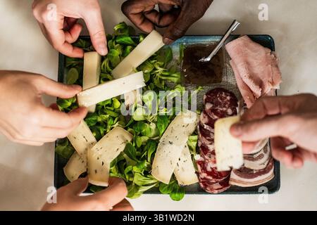 Verschiedene Freunde teilen sich eine Käse- und Wurstplatte und genießen gemeinsam ein geselliges kulinarisches Erlebnis. Inklusion, soziale Mahlzeit, Multikultu Stockfoto