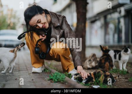 Lächelnde Frau, die Zeit mit Straßenkatzen in einem Stadtviertel genießt Stockfoto