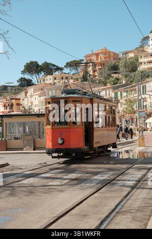 Traditionelle rote Straßenbahn, die durch eine malerische Straße mit historischen Gebäuden auf einem Hügel in einer mediterranen Stadt auf Mallorca fährt. Stockfoto
