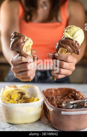 Nahaufnahme von zwei Eiskegeln, die von einer jungen Frau gehalten werden, wobei das Eis leicht zwischen ihren Fingern schmilzt. Konzentriere dich auf die Schaufeln, außer Fokus hinten Stockfoto
