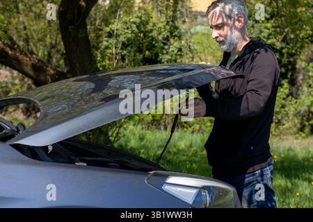Bärtiger Mann, der vor einer offenen Autohaube steht. Panne des Fahrzeugs Stockfoto