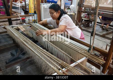 Ein Seidenraupenmaschinist, der einen Weber im „Thai Silk Village“ in Ban Sanuan NOK, einem Dorf in der Nachbarschaft von Chiang Mai, dem thailändischen seco, betreibt Stockfoto