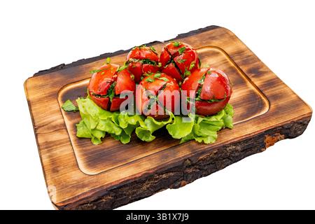 Fünf gegrillte Tomaten sind kunstvoll auf einem Bett aus knusprigem Salat angeordnet. Frische Kräuter setzen leuchtende grüne Akzente und betonen das farbenfrohe Geschenk des Gerichts Stockfoto